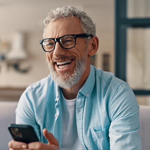 A mature man with beard smiling while holding phone