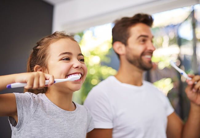 A child and her father brushing their teeth